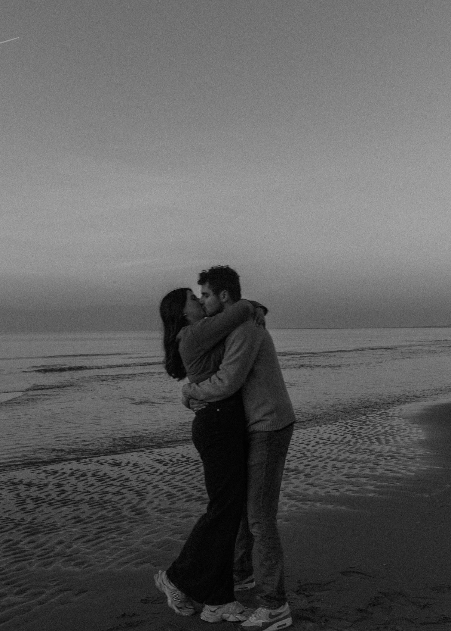 Silhouettes embrace on a moody beach at sunset creating a romantic scene.