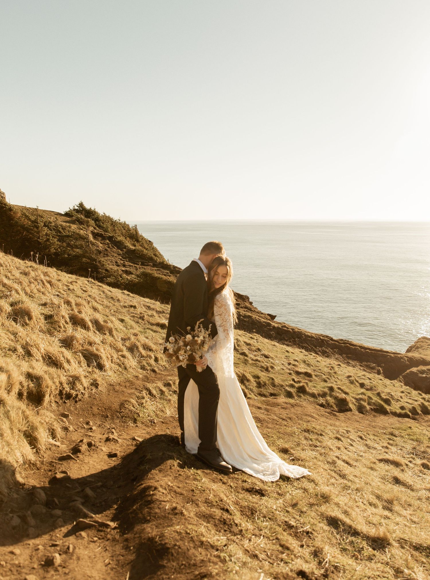 A couple shares a romantic moment on a rocky coastal cliff overlooking the ocean at sunset.