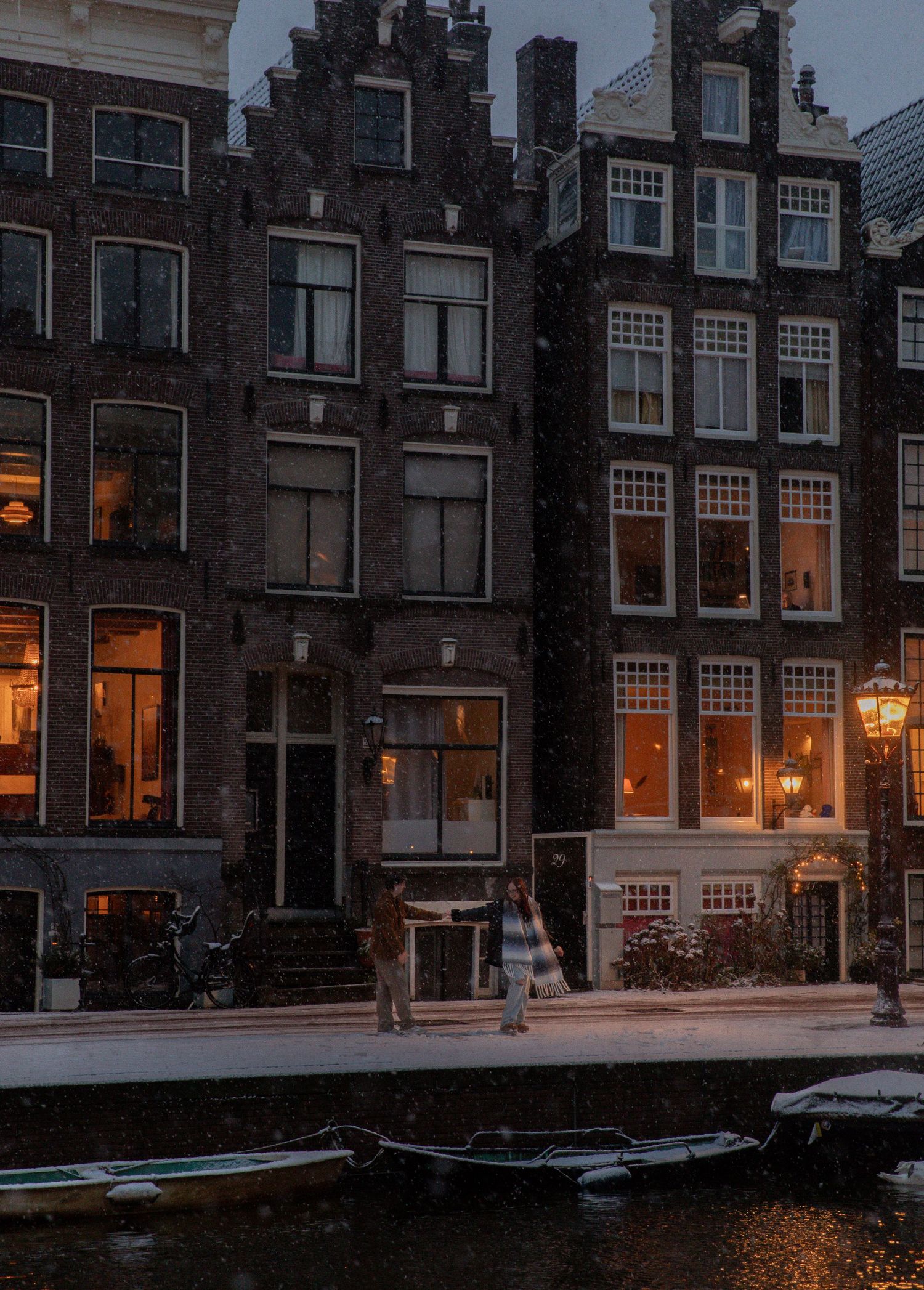 Historic Amsterdam canal at dusk with illuminated windows reflecting in dark water.
