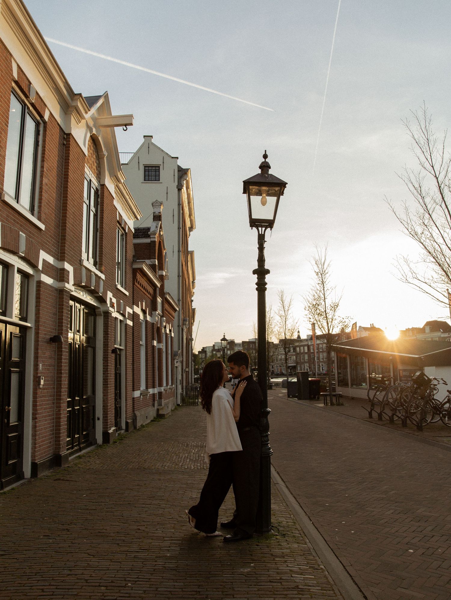 Couple kissing by a vintage street lamp at golden hour on a cobblestone street in Amsterdam.