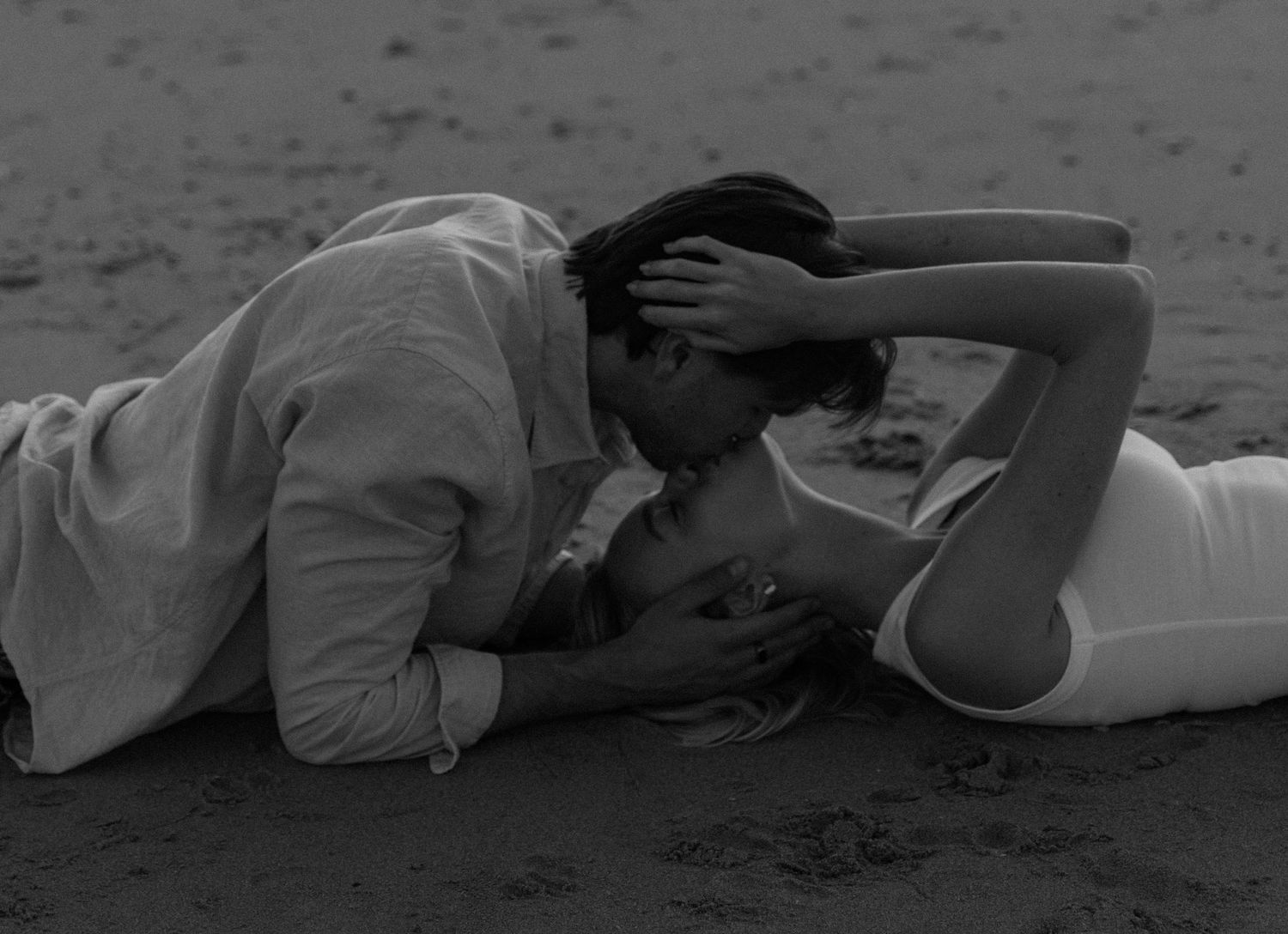 Black and white photo of a couple sharing a romantic kiss on a sandy beach.
