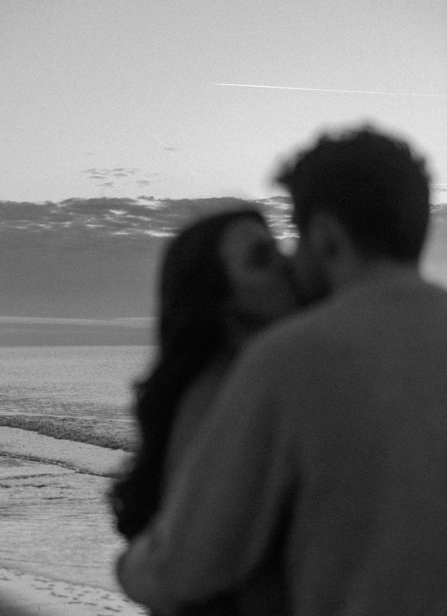 Silhouettes against an ocean backdrop share an intimate moment at dusk.