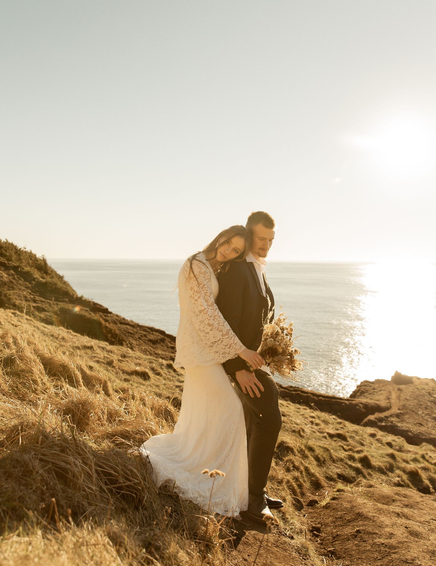 Couple embraces on scenic coastal cliffs at sunset with ocean waves crashing below.