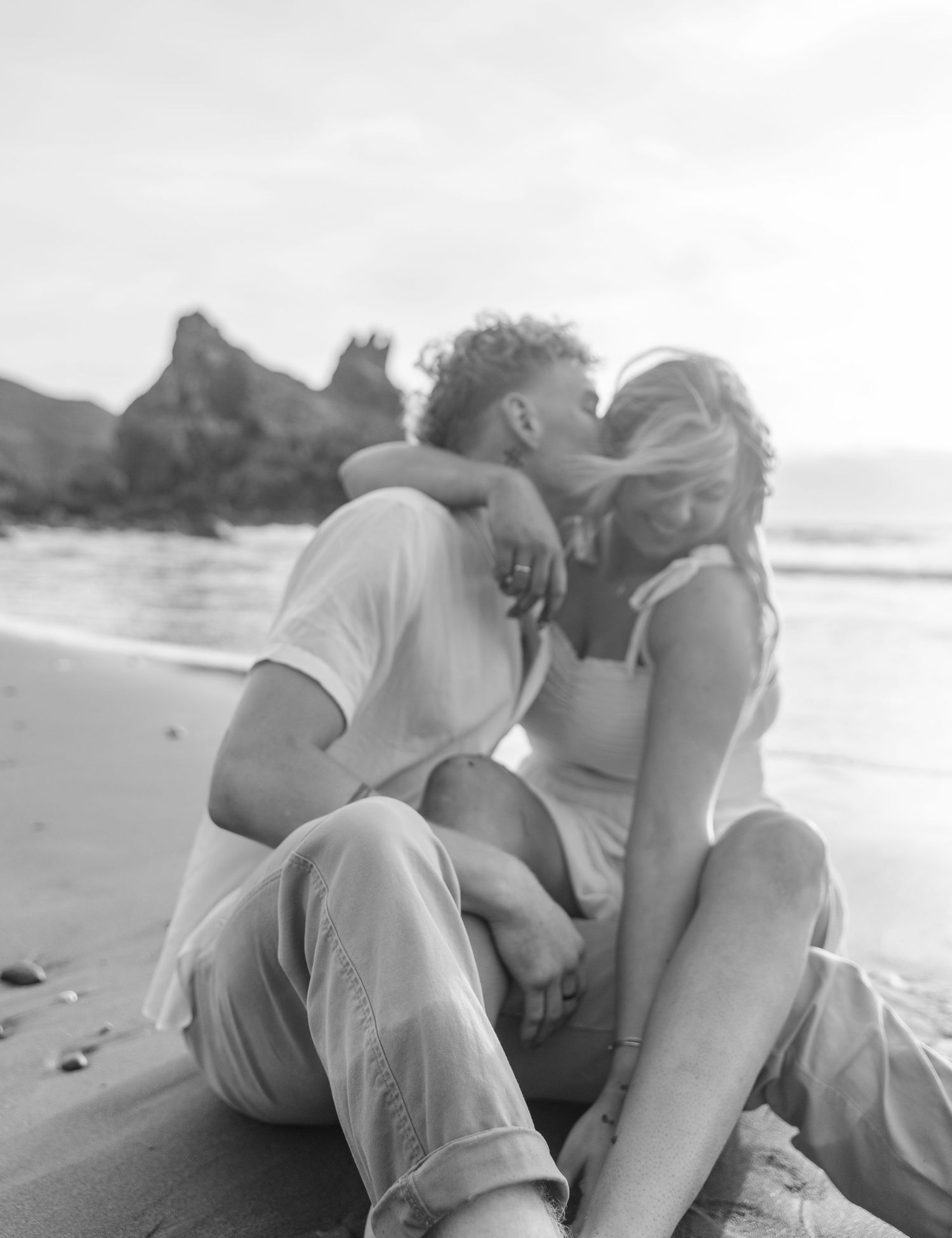 Romantic couple lying together on a sandy beach at sunset in black and white photography.