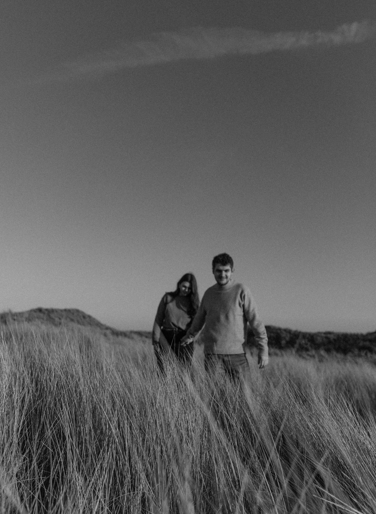 Figures walking through tall grass on coastal dunes in black and white.