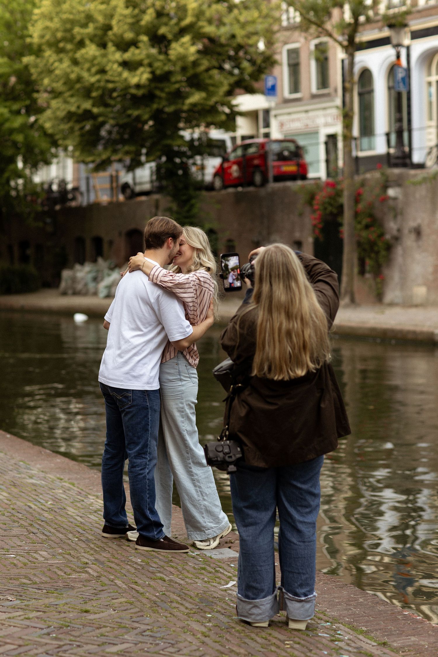 A photographer captures a couple kissing by a canal in Utrecht, Netherlands, on a cloudy day.