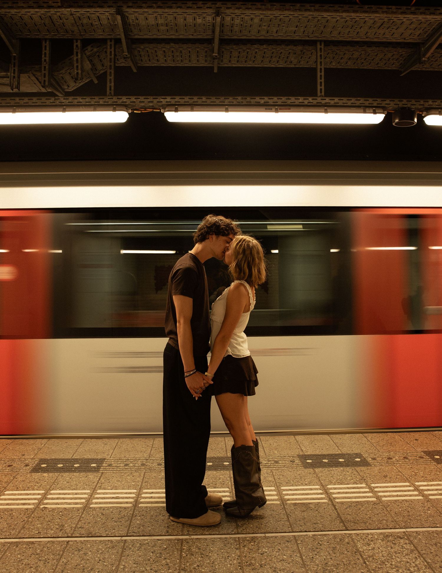 Couple kissing on subway platform as red train speeds by in motion blur.