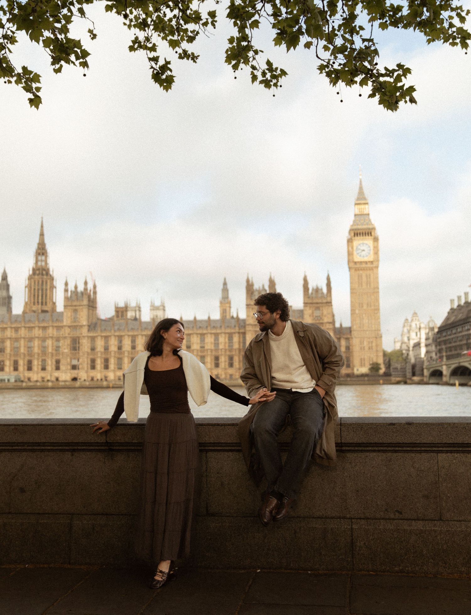 Couple conversing by the Thames with Big Ben and Houses of Parliament backdrop in London.
