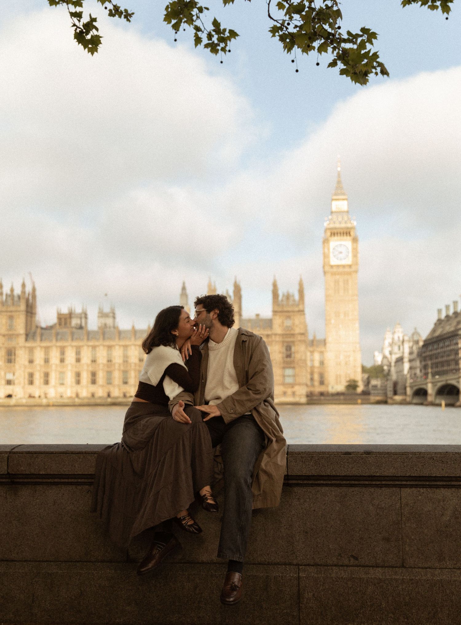 Couple sharing a romantic moment on the Thames embankment with Big Ben and Parliament in London backdrop.