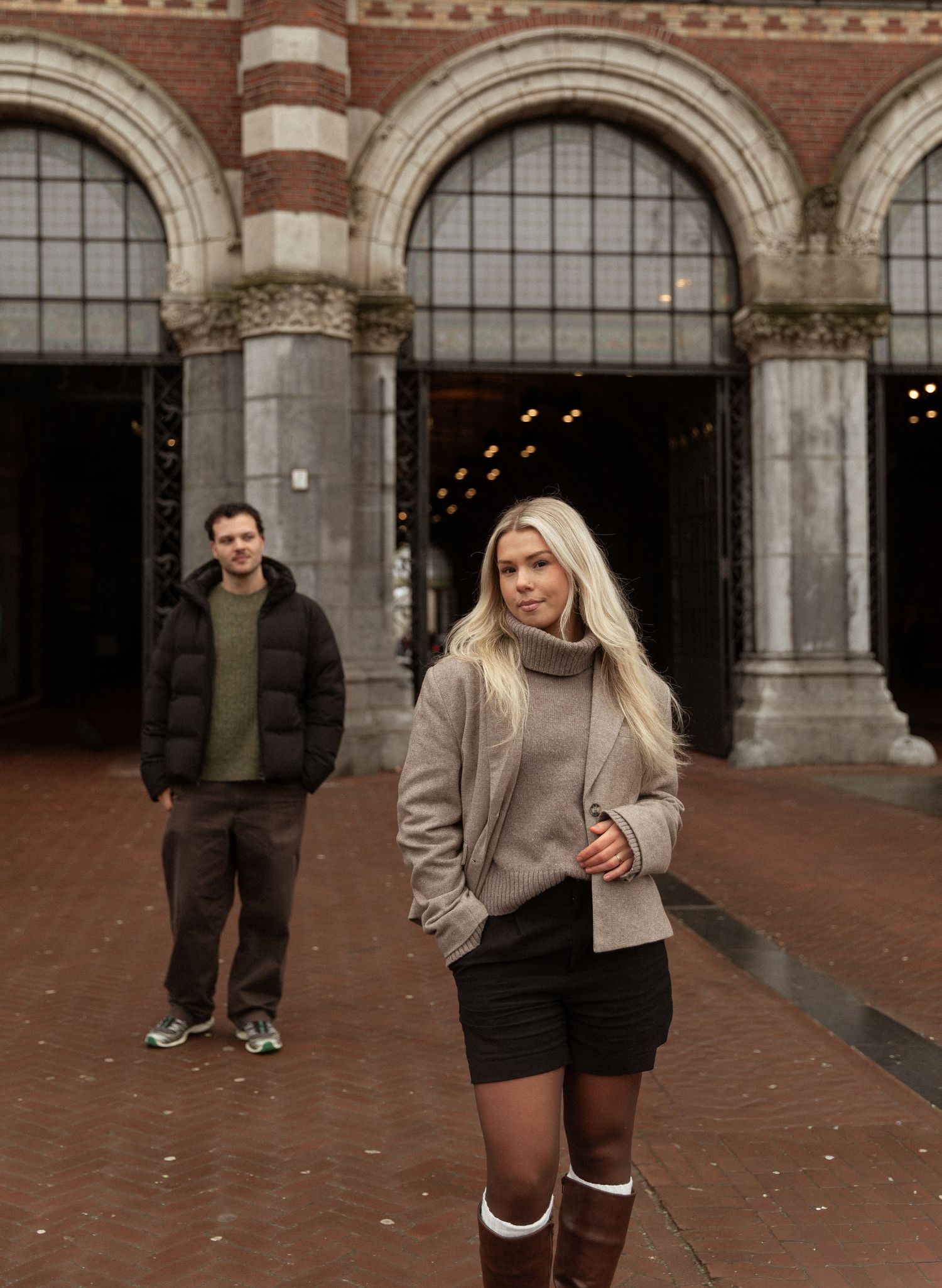 A sequence of photos showing someone in a beige jacket and black shorts walking and posing in front of a brick building.