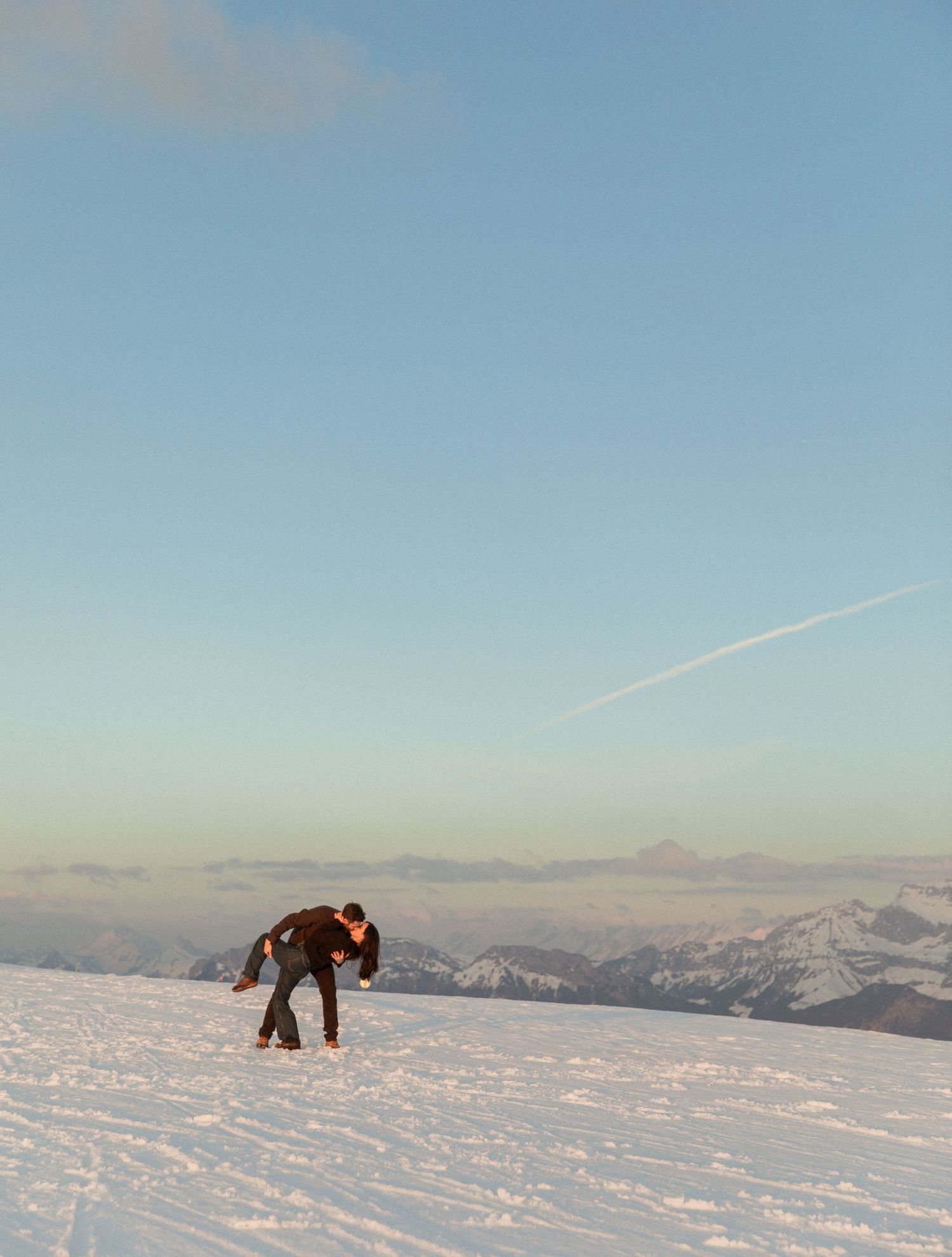 A panoramic sequence of snowy mountain landscapes with a person bent over in the distance against a clear blue sky.