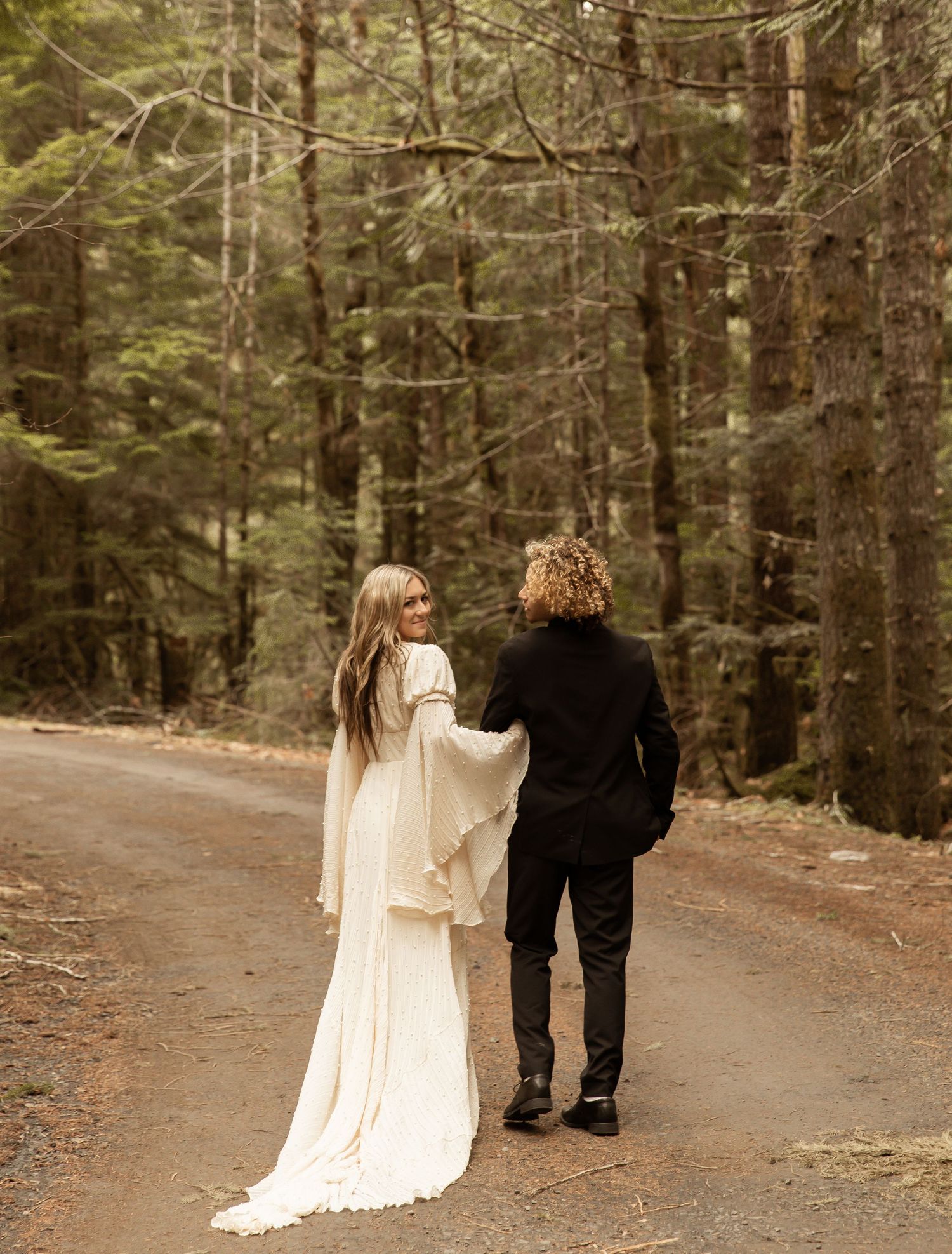 A couple walks together on a forest trail during their wedding photoshoot.