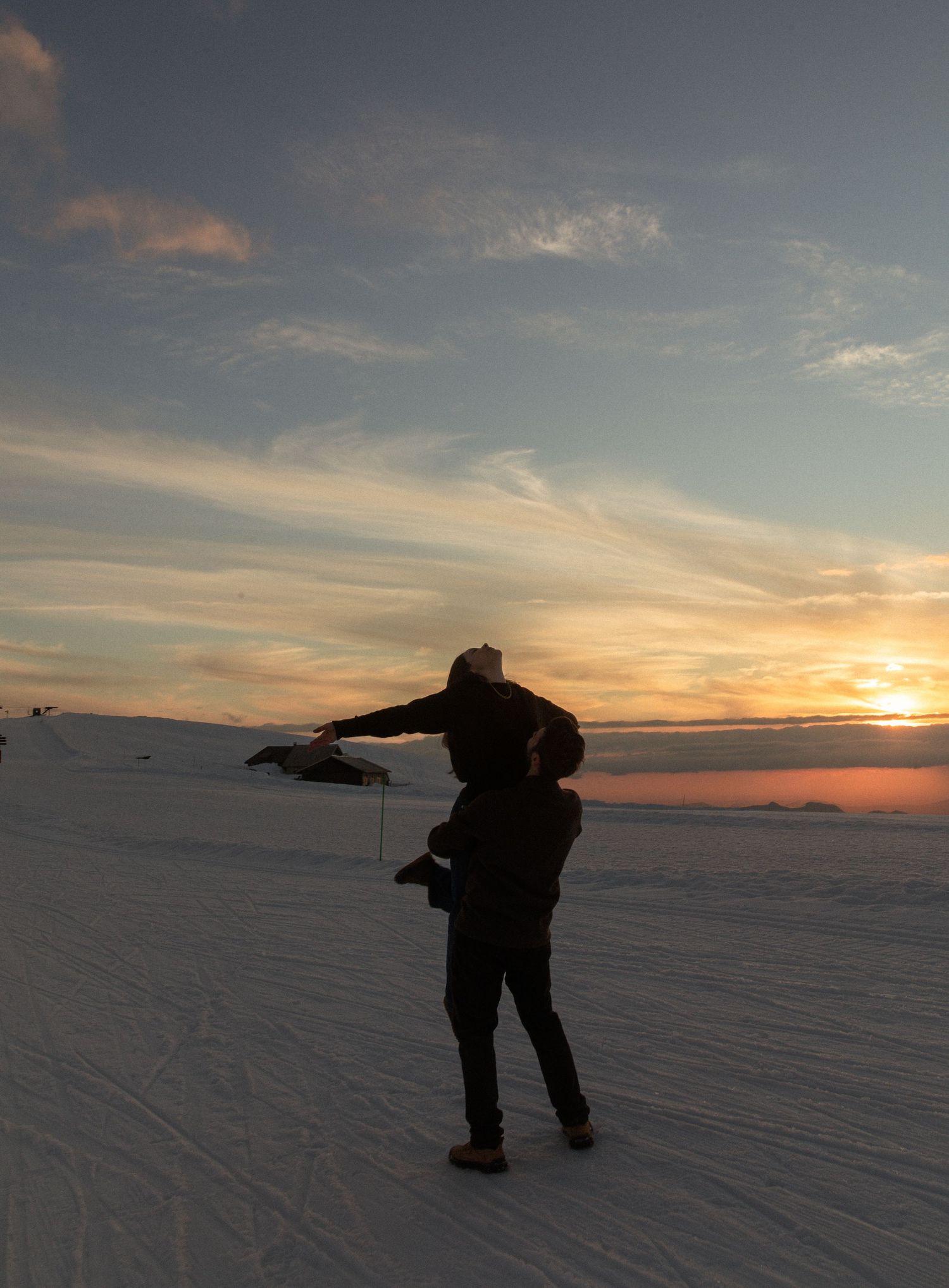 Silhouette of person with outstretched arms stands on snowy landscape against dramatic sunset sky.