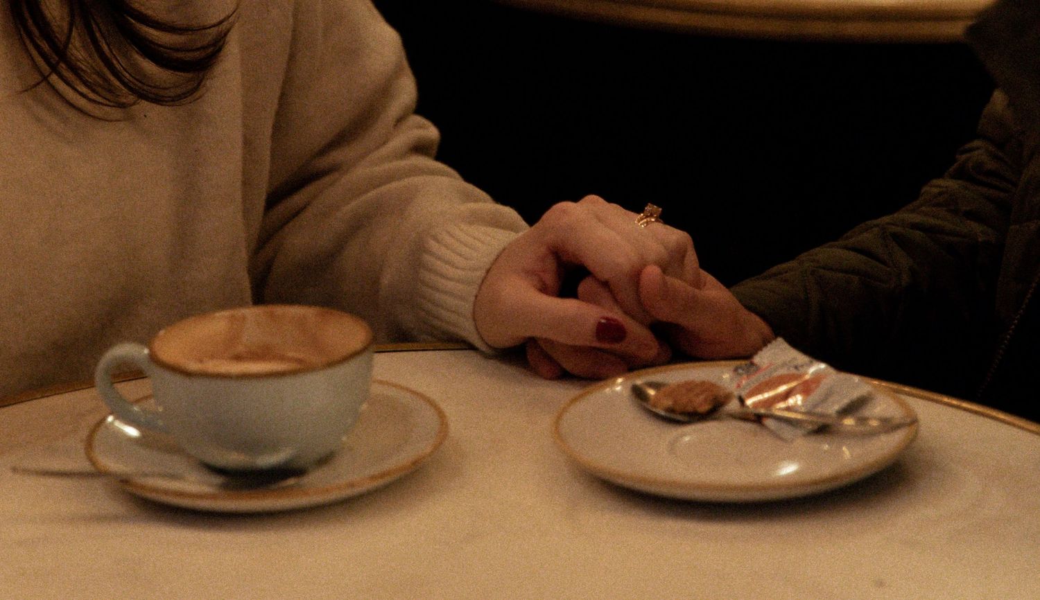 Coffee cups and hands on a dark wooden table in an intimate cafe setting.