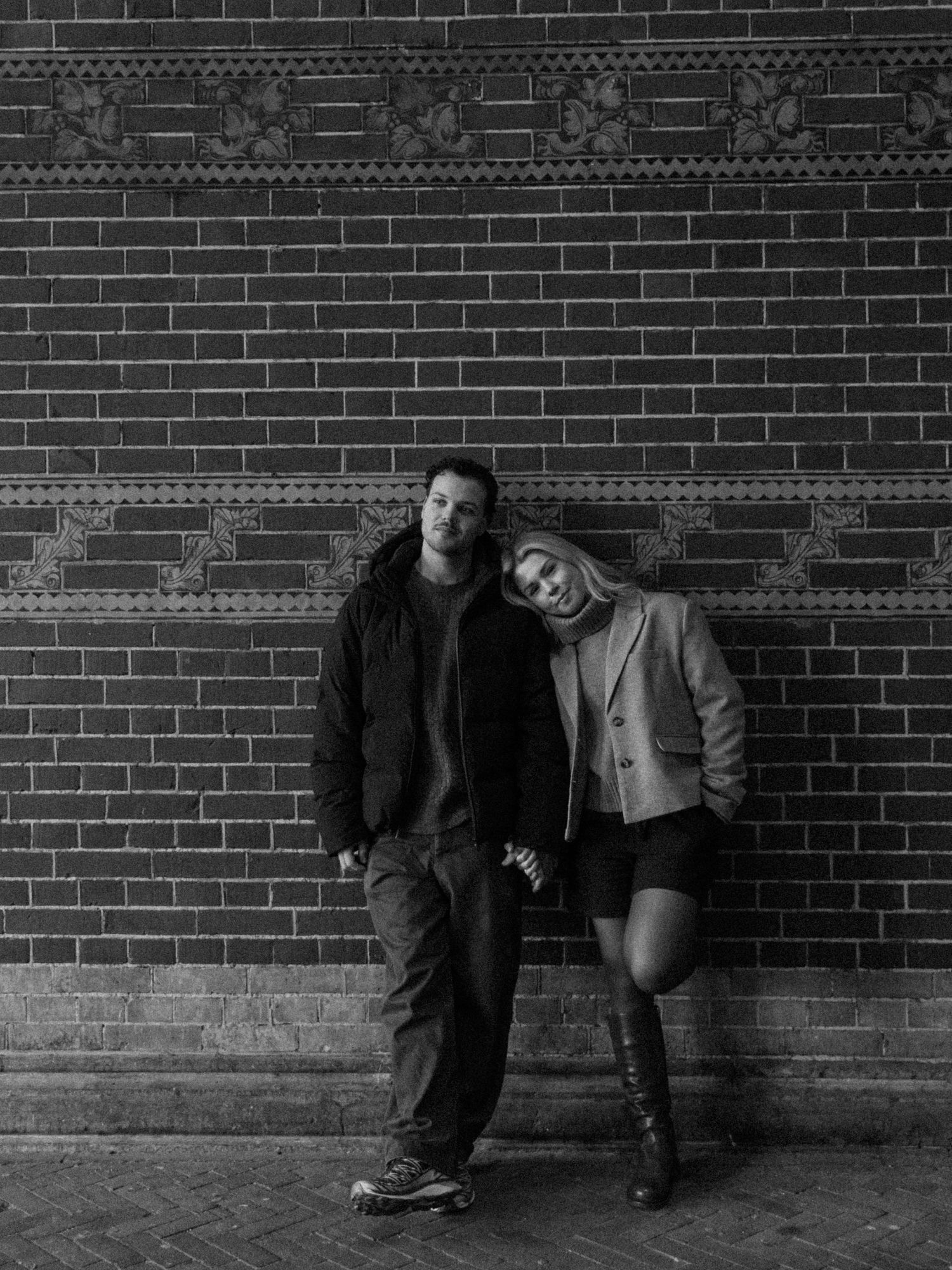 Black and white series of candid portraits against a brick wall showing playful poses and interactions.