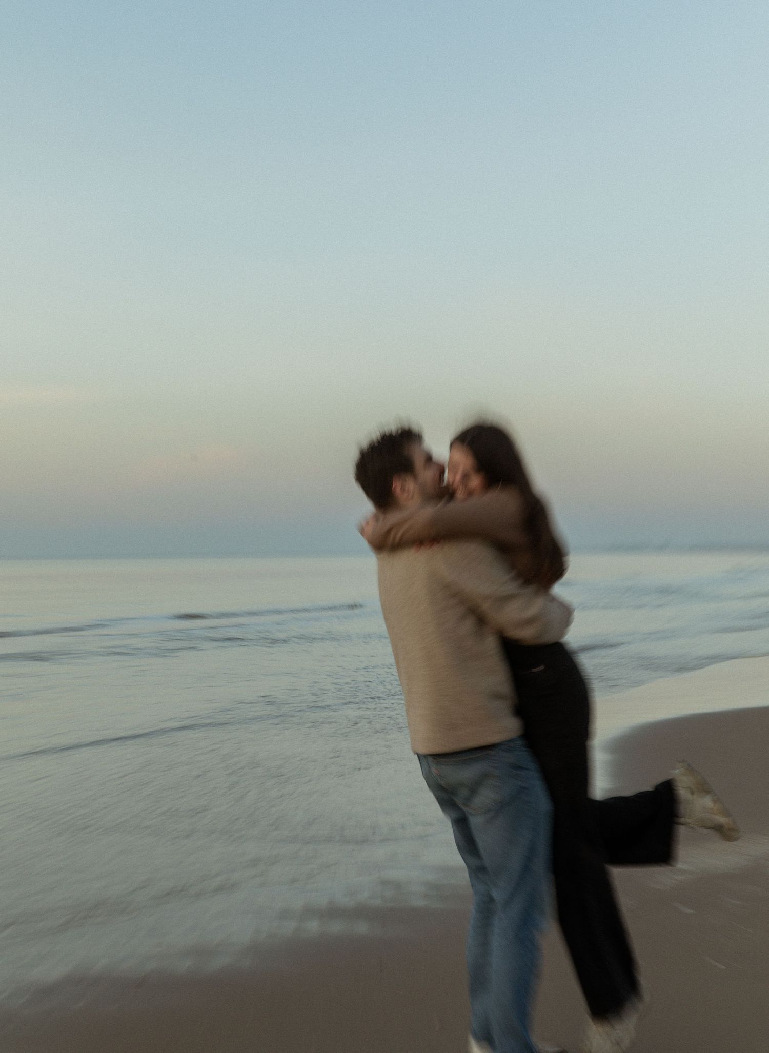 A couple embracing and spinning on a beach at dusk.