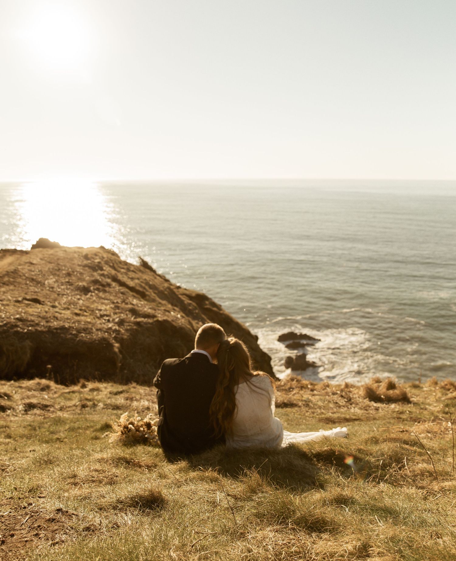 Someone sits on a grassy coastal cliff overlooking a misty ocean during golden hour.