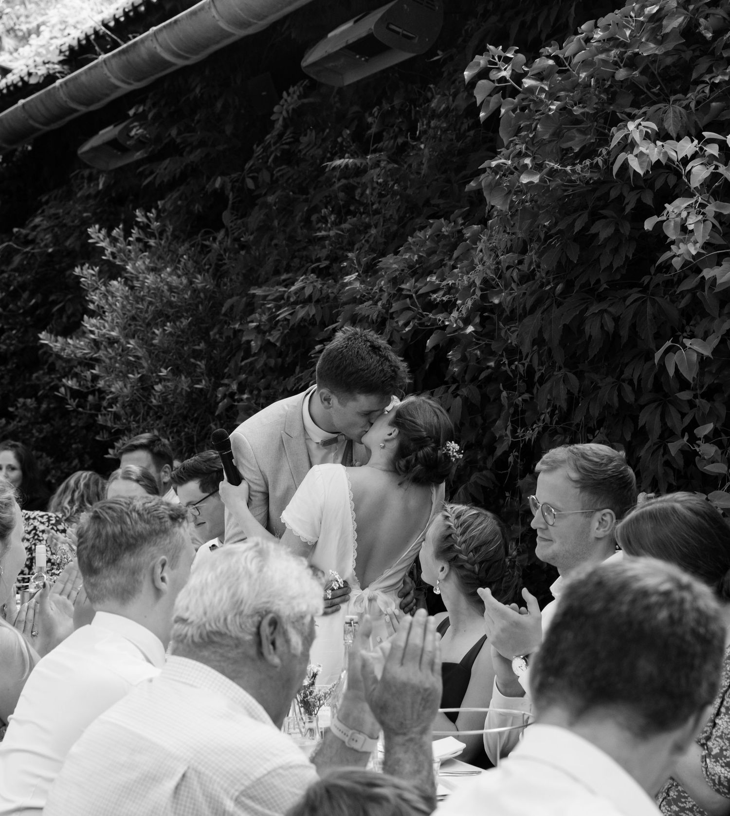 A black and white wedding celebration scene with guests gathered outdoors.