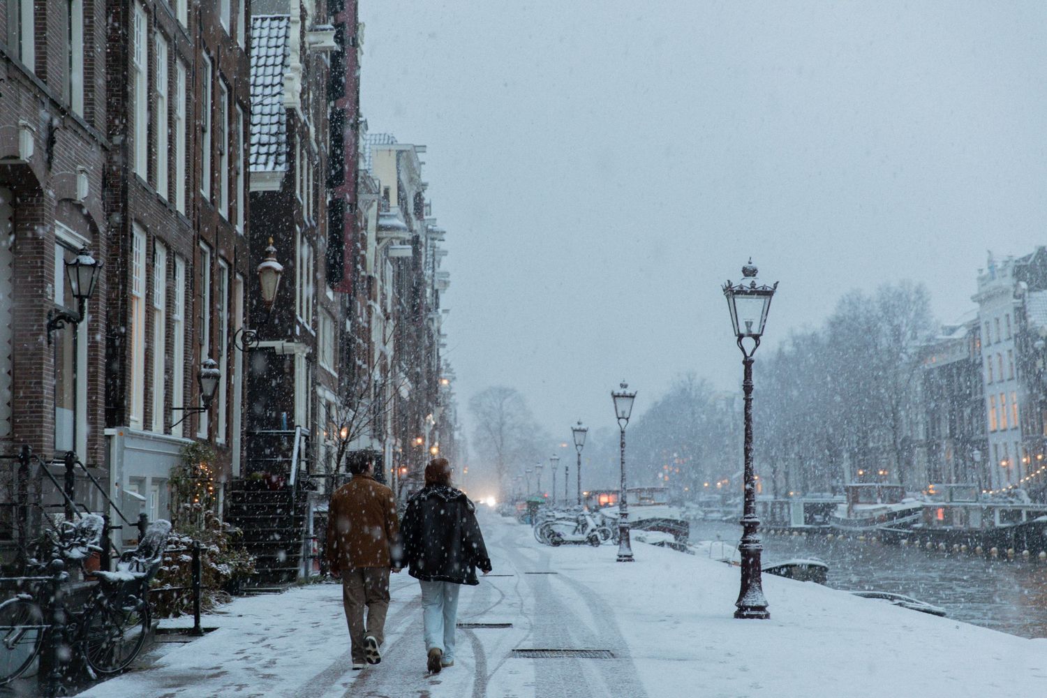 Snowy winter scene on an Amsterdam street with historic buildings and lampposts.