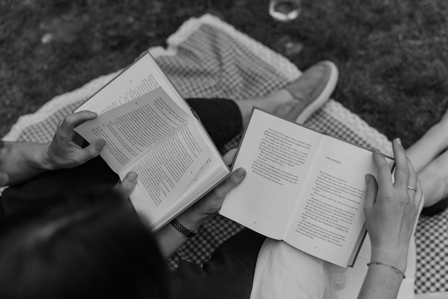 Two people relaxing outdoors reading open books side by side in a black and white photo.