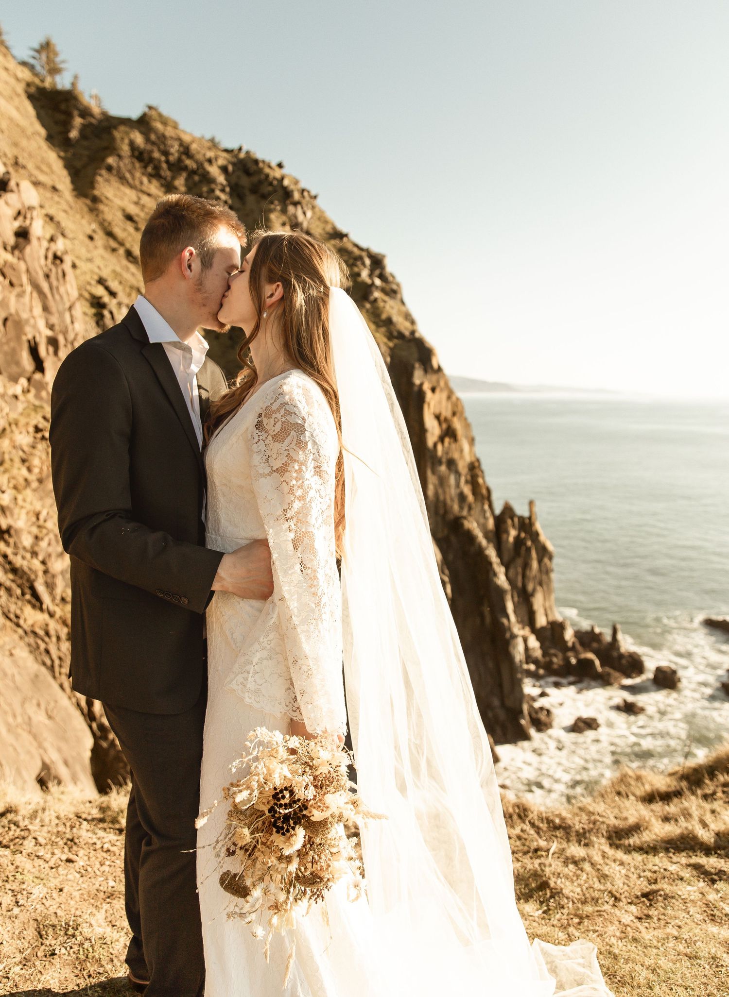 A couple shares an intimate moment during their coastal cliff wedding ceremony at sunset with ocean views.
