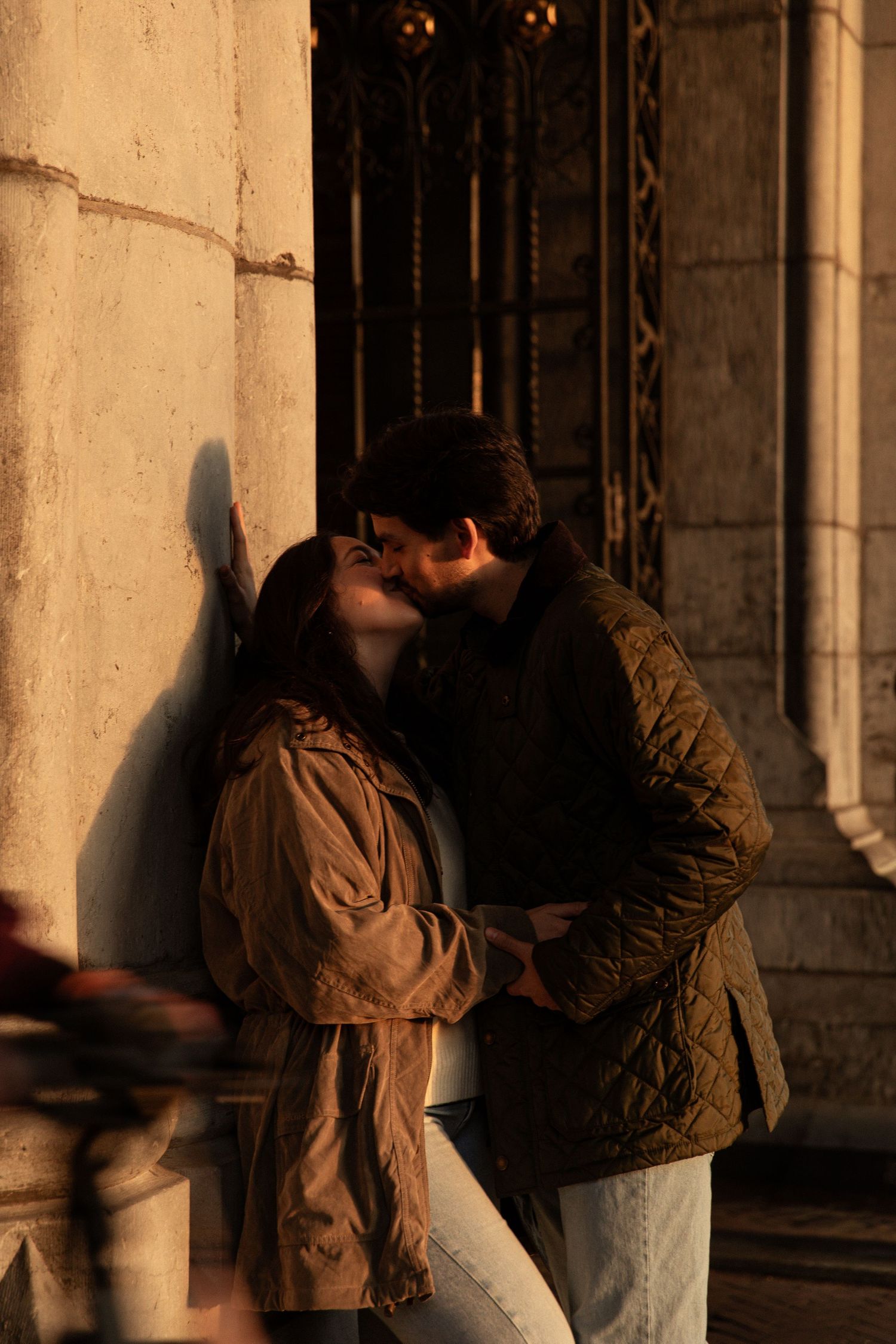 A tender moment between two people embracing against a warm-toned wall at sunset.