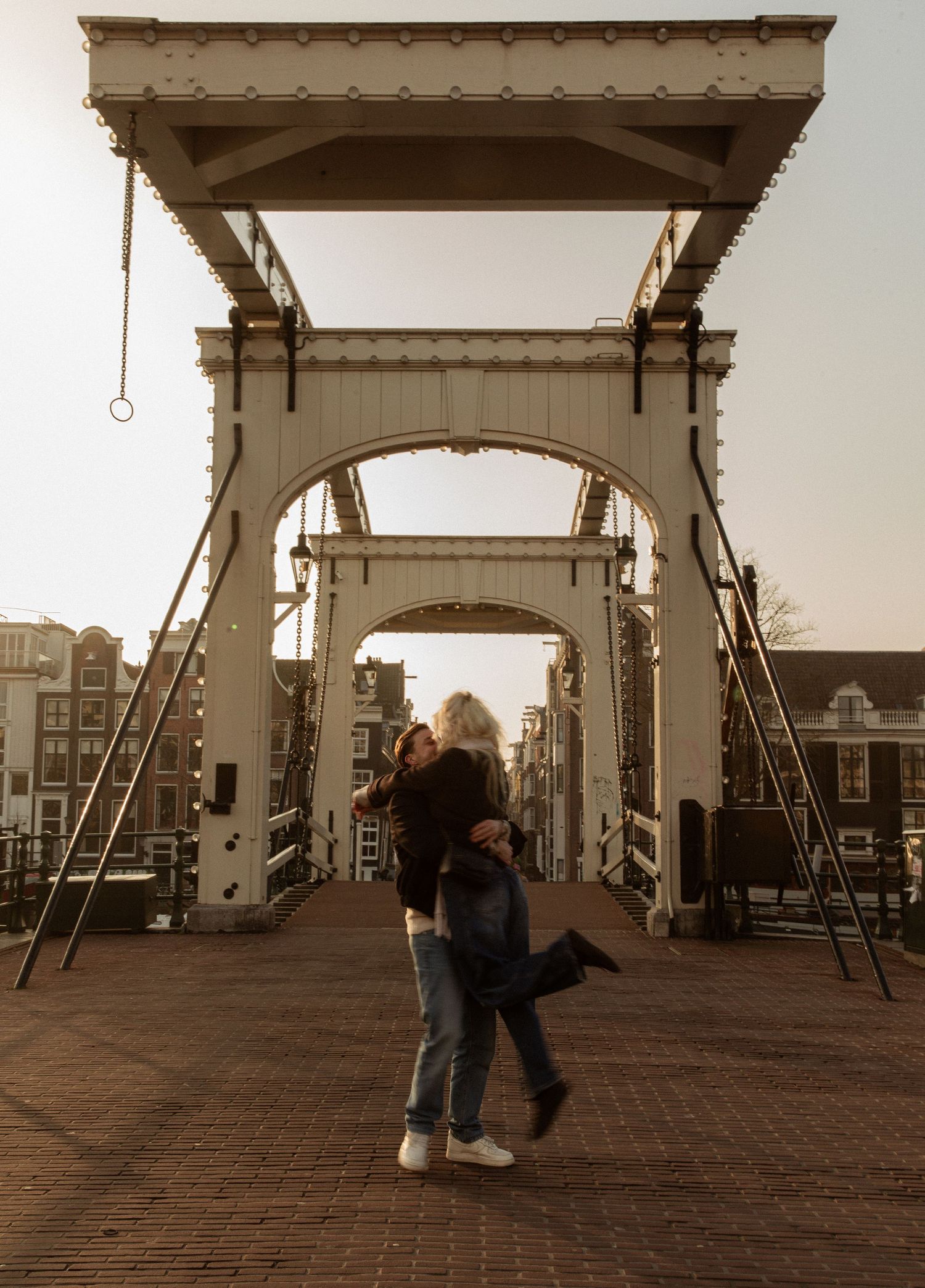 A couple embraces on Amsterdam's historic Skinny Bridge (Magere Brug) during sunset, with its iconic wooden architecture.