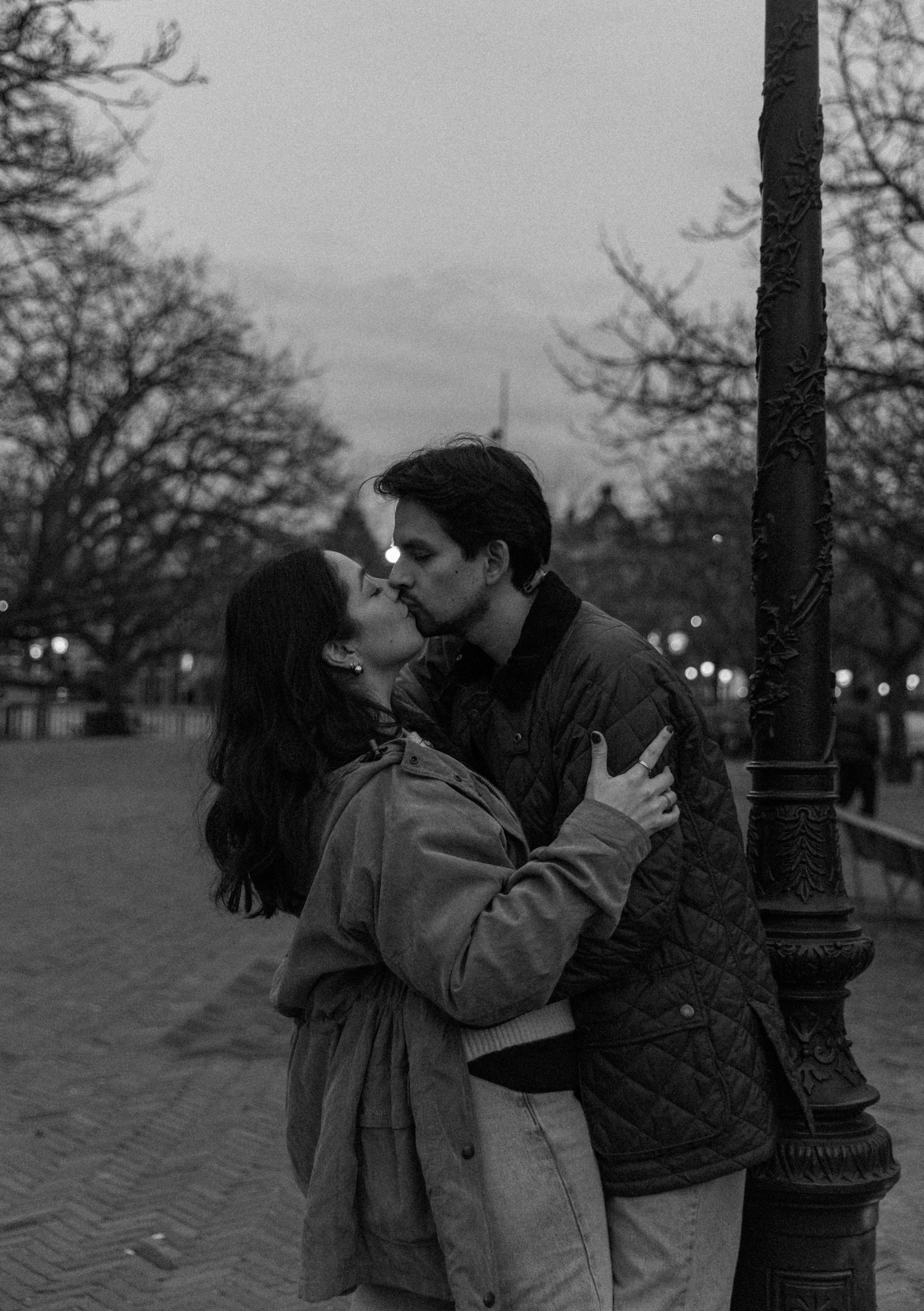 Black and white romantic photos of a couple sharing intimate moments near a lamppost in a park.