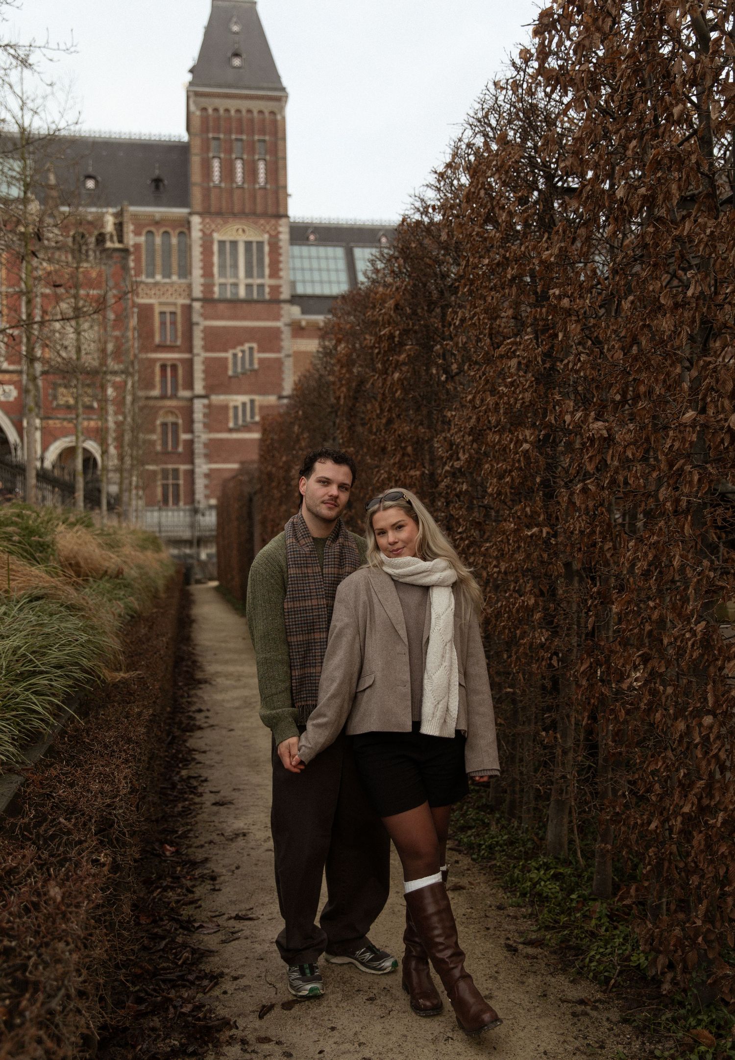 A walking path lined with autumn hedges leads to a historic brick building.