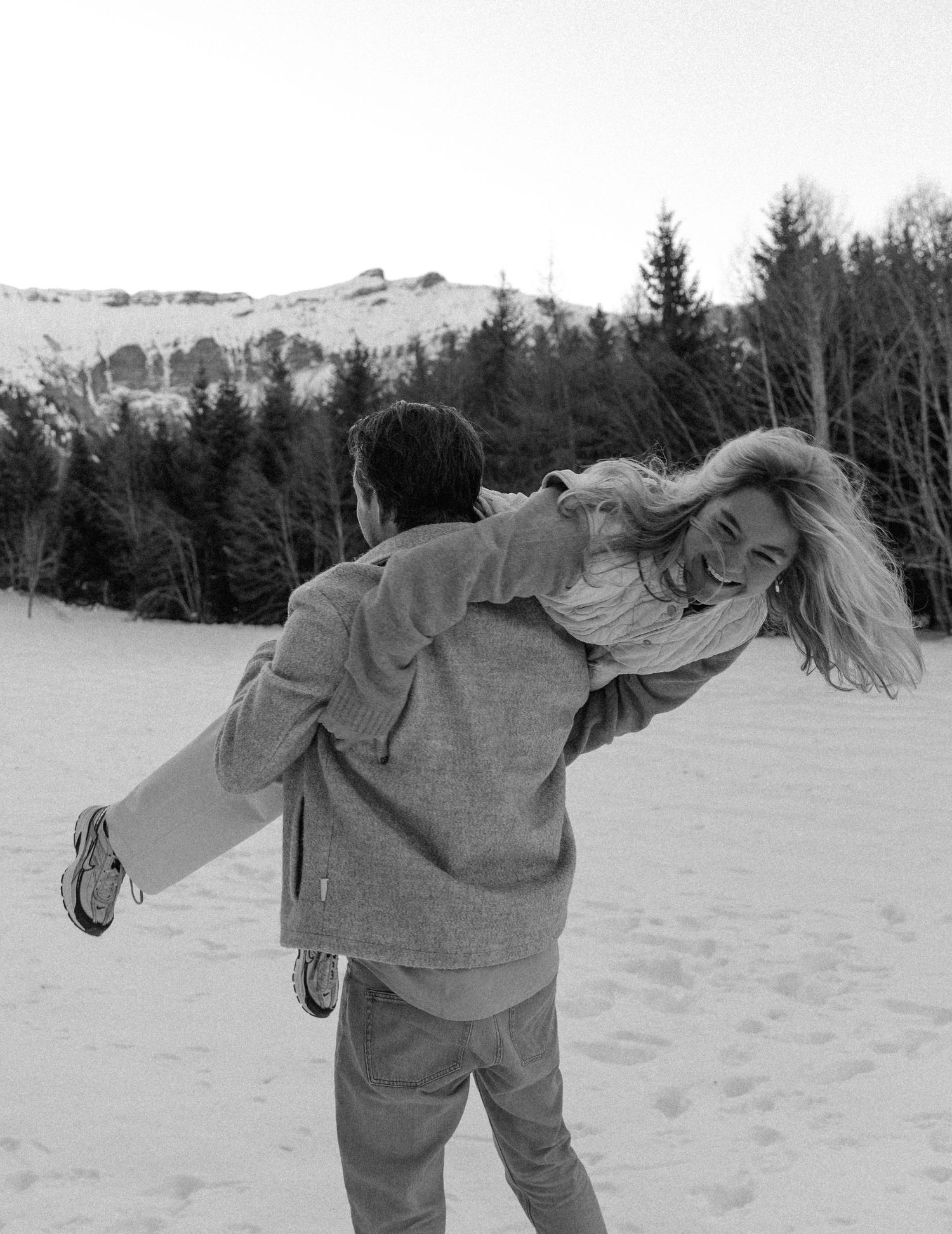 A playful moment captured in black and white as someone carries another person in the snow.