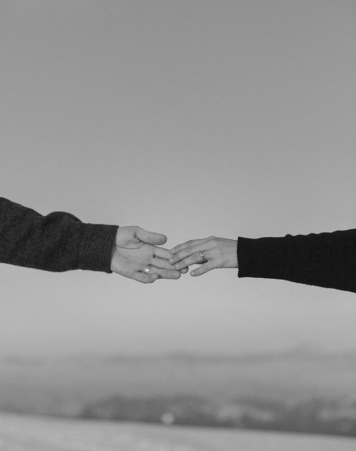 Two hands reaching towards each other against a blurry background in black and white photography.