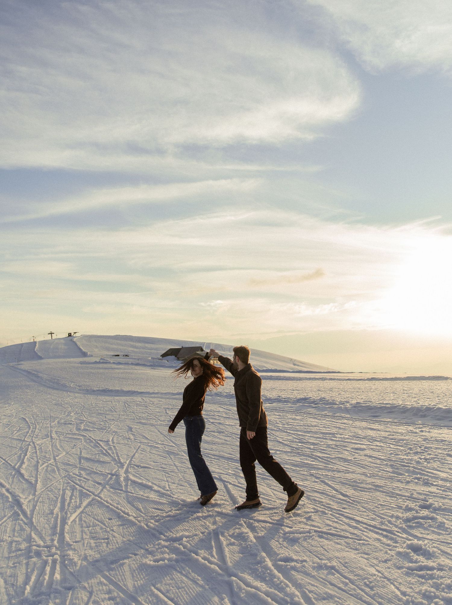 Silhouettes of skiers gliding across a snowy slope against a cloudy winter sky at sunset.