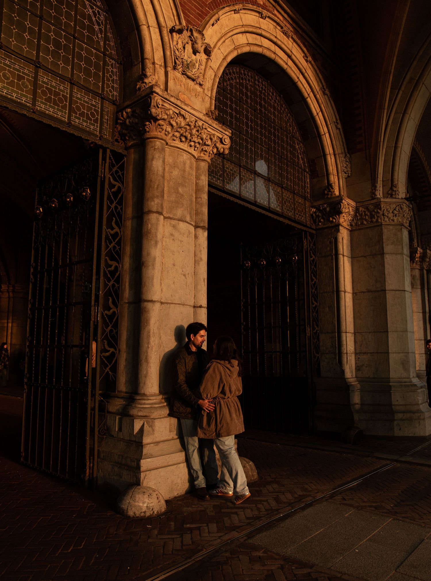 Two silhouettes embrace in an ornate archway at night.