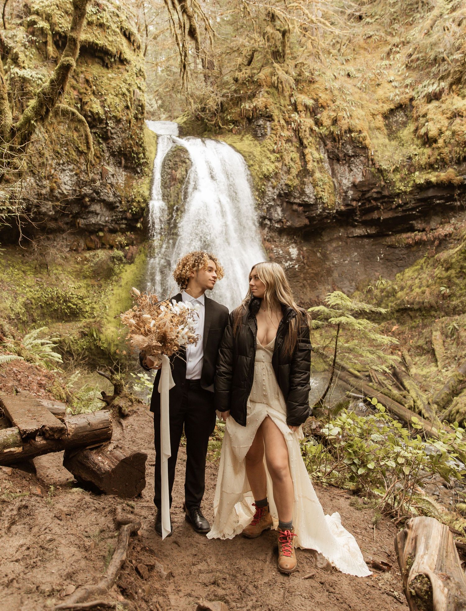 Romantic waterfall elopement scene with couple in formal attire against rocky cliffs.