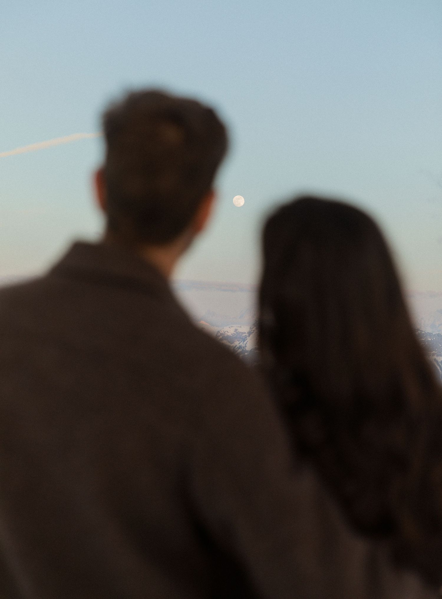 Silhouetted figures stand together against a light blue sky background during sunset or sunrise.