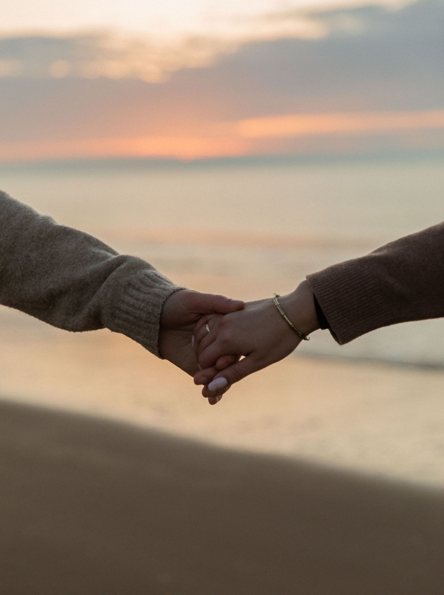 Two hands reaching towards each other against a sunset sky background in a romantic gesture.