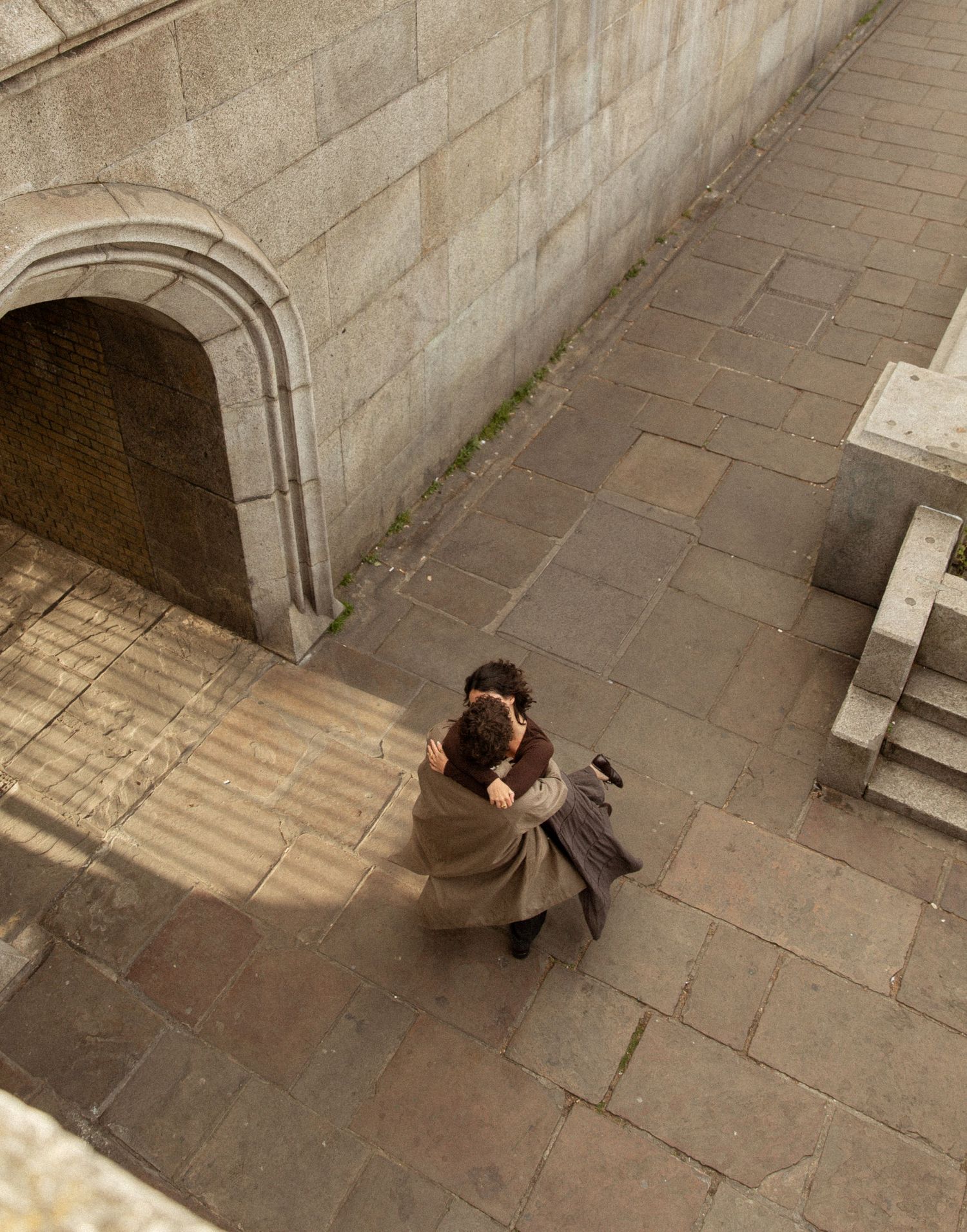 Aerial view of a person in a beige coat photographing a stone courtyard with an arched doorway.
