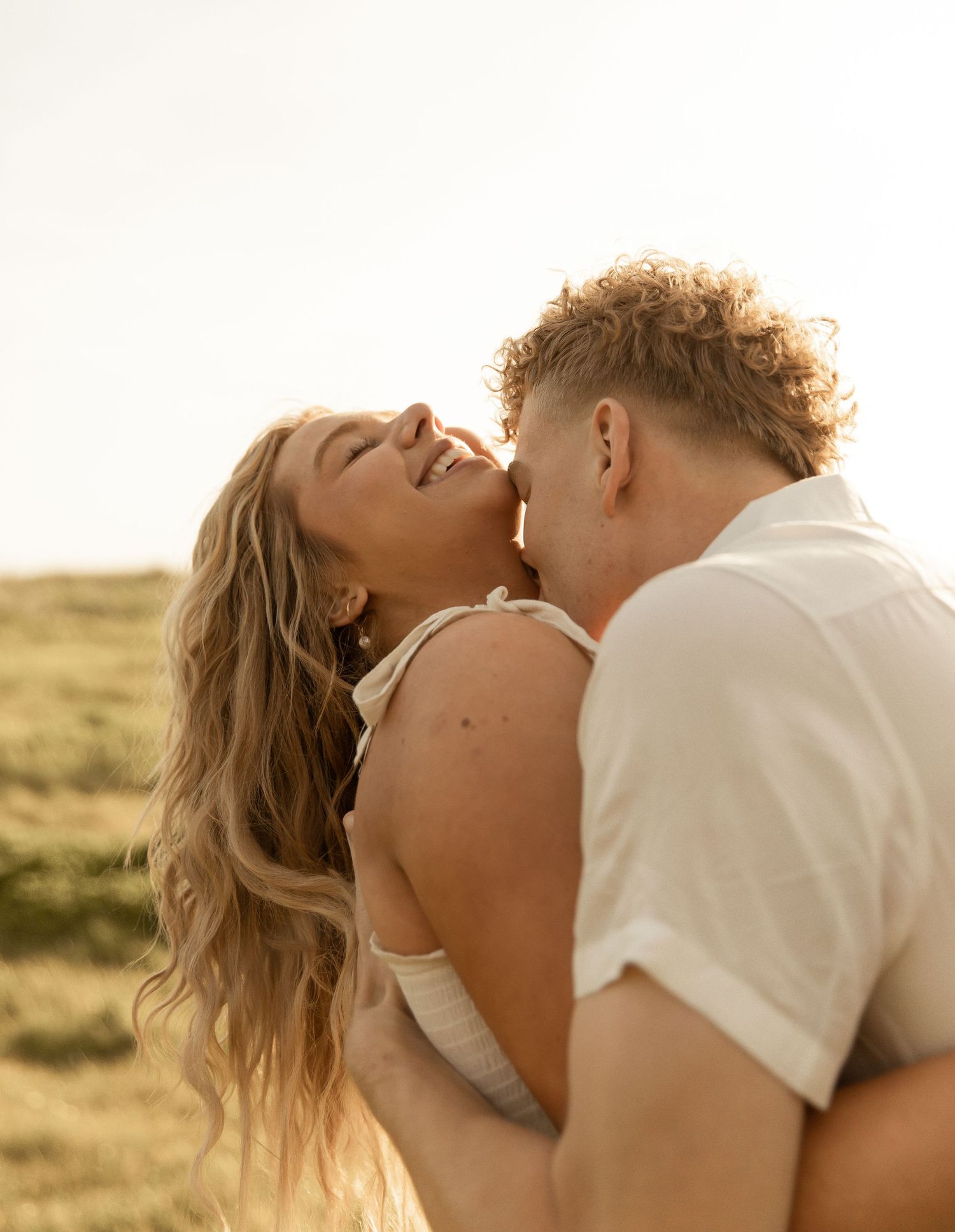 A romantic couple embraces and kisses passionately in a golden field at sunset.