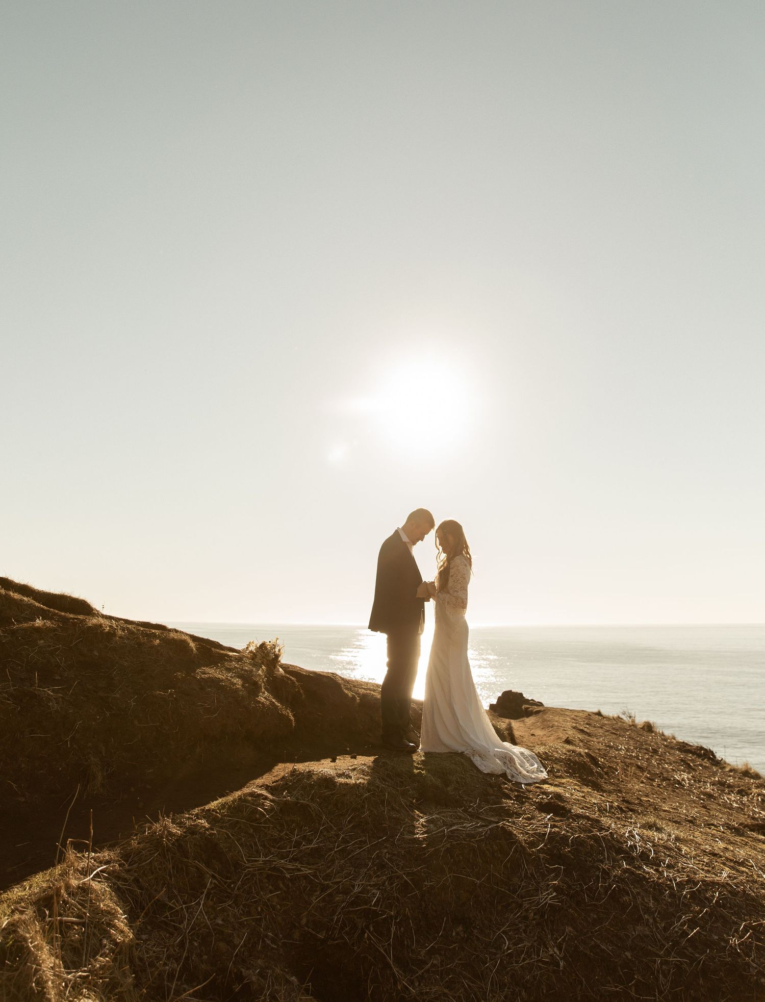 A silhouetted couple shares an intimate moment on a cliff overlooking the ocean at sunset.