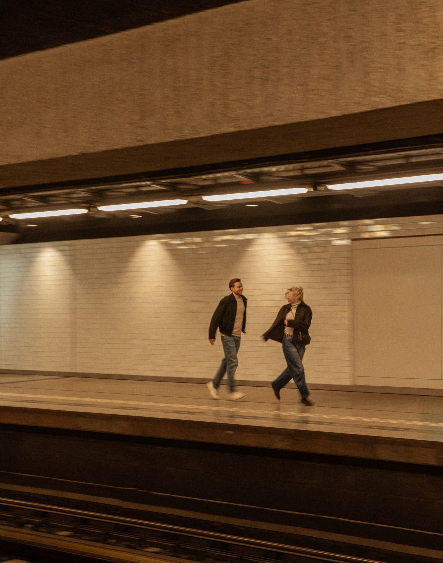 A sequence of motion-blurred figures moving through a dimly lit underground subway tunnel or passageway.