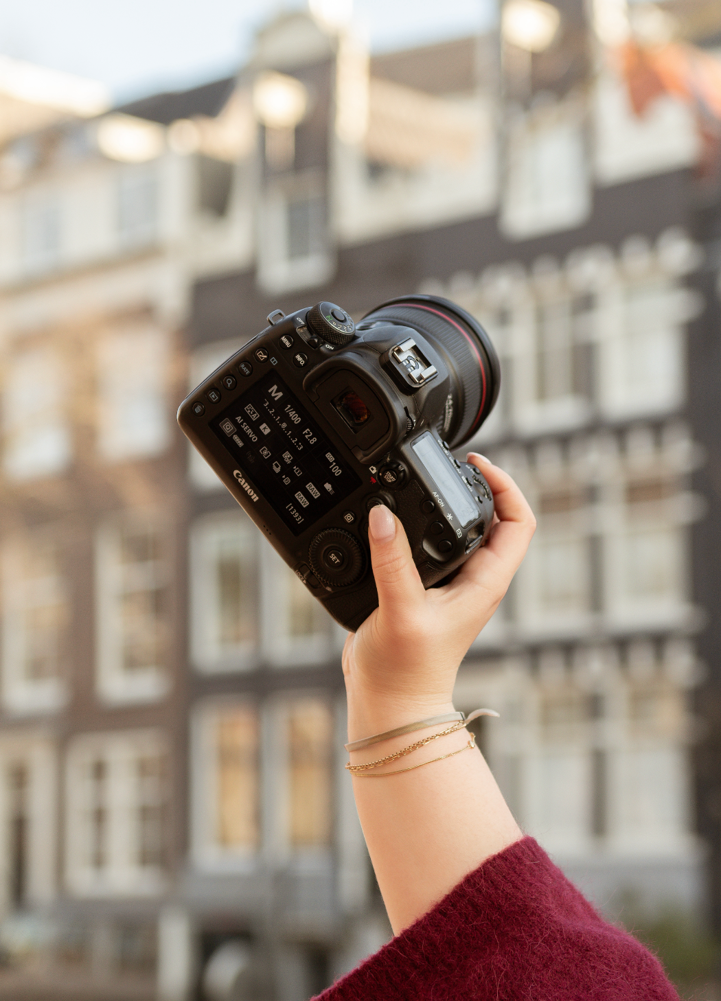 Close-up of hands holding professional camera lens against urban backdrop.