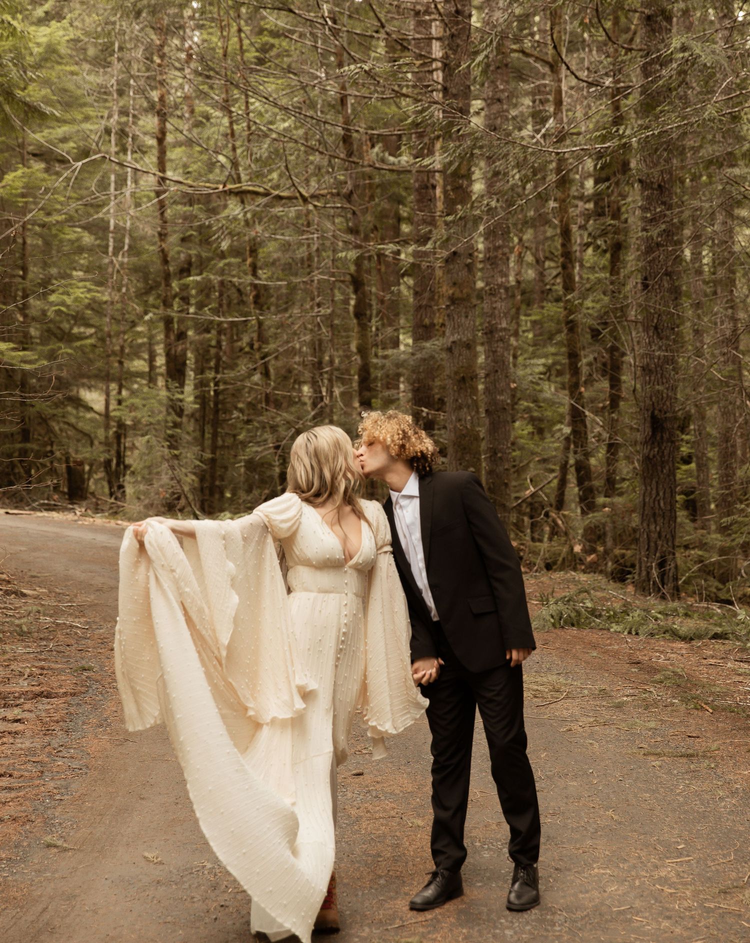 Wedding couple walking hand in hand through evergreen forest.