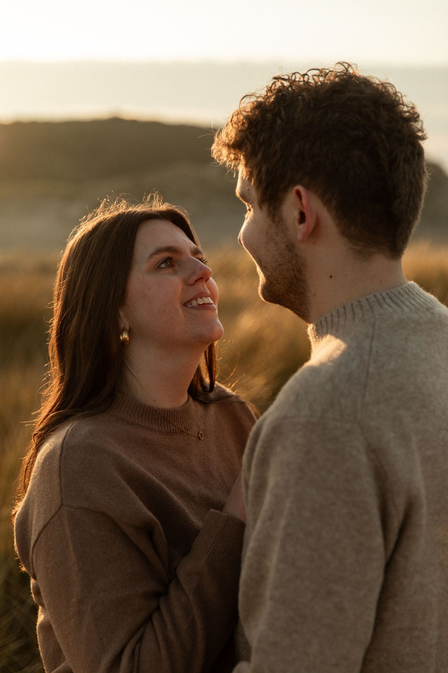 A couple in warm sweaters sharing an intimate moment at sunset.
