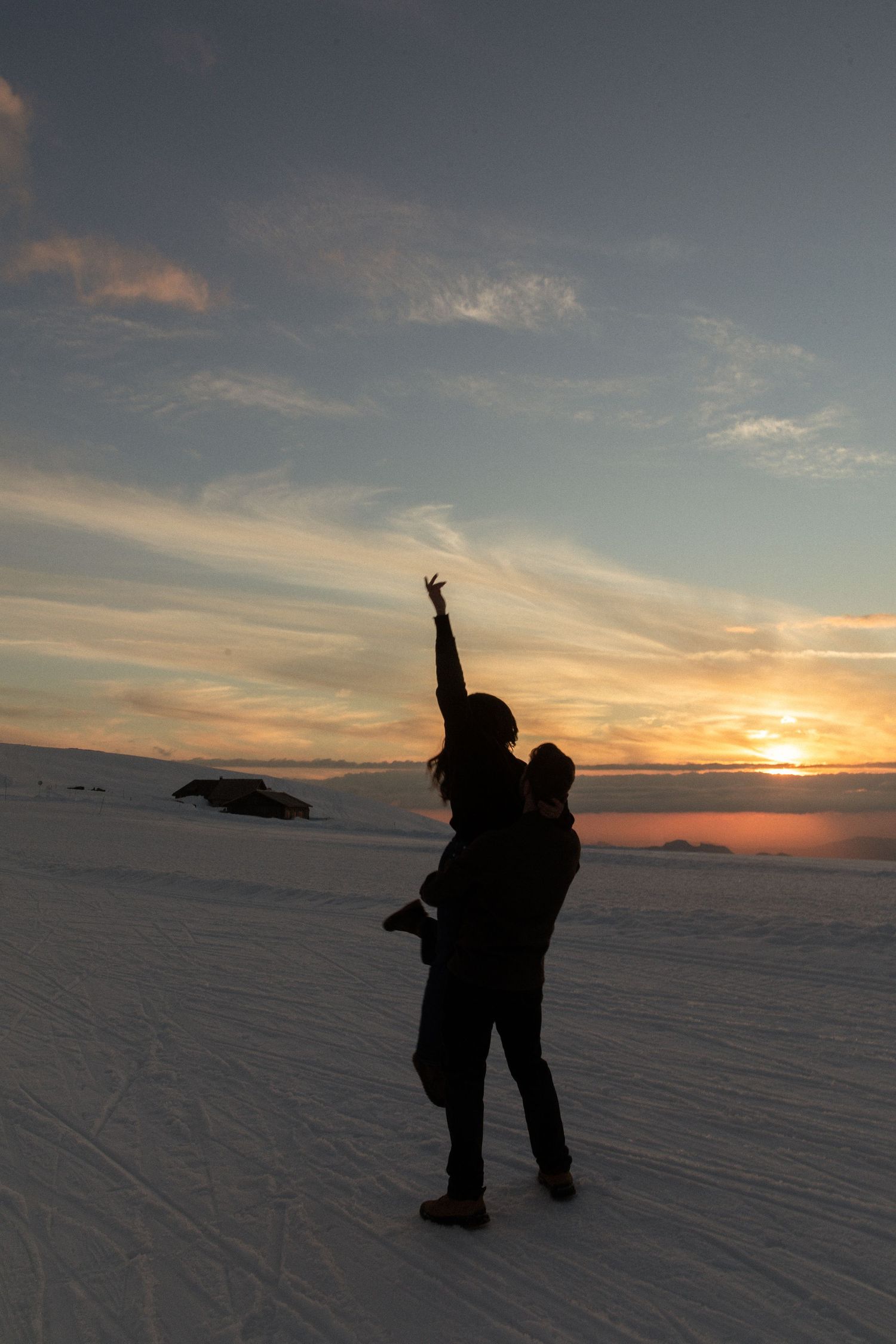 Silhouetted figure stands against dramatic sunset on snowy winter landscape with colorful sky and clouds.