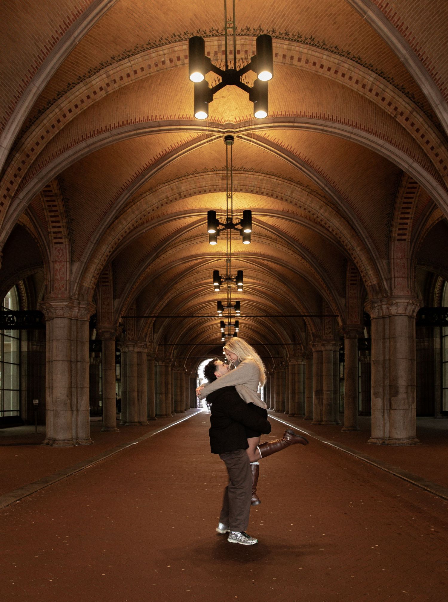 Two dancers perform a graceful lift sequence in an ornate arched hallway with decorative lighting and architecture.