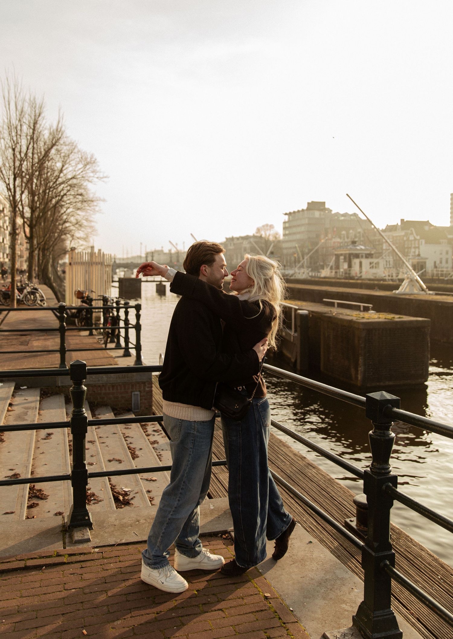 A romantic couple shares a tender moment along a misty waterfront boardwalk in a series of sepia-toned photographs.