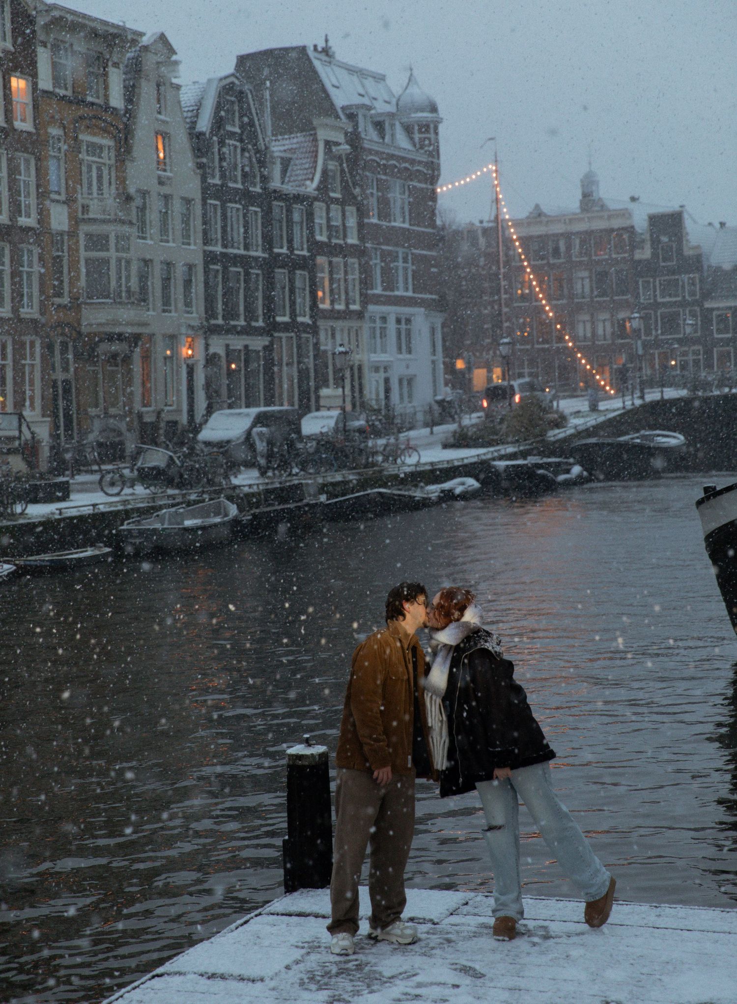 A snowy evening along Amsterdam's canals with historic buildings and twinkling lights in the background.