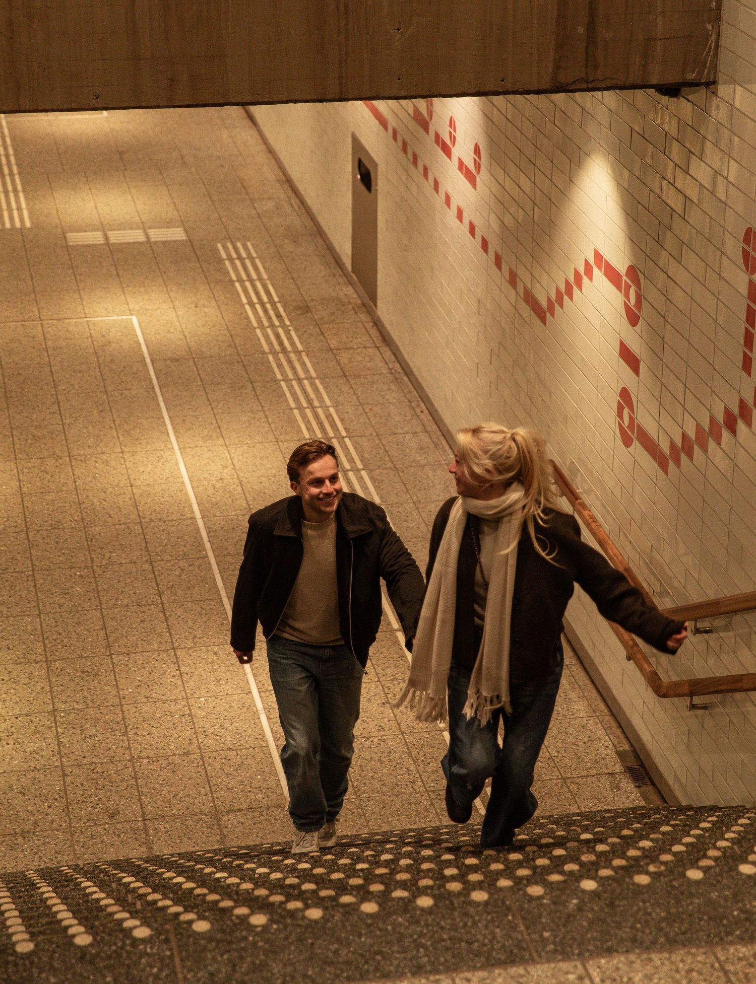 A sequence of images showing two people walking down a tiled subway station staircase in a synchronized manner.