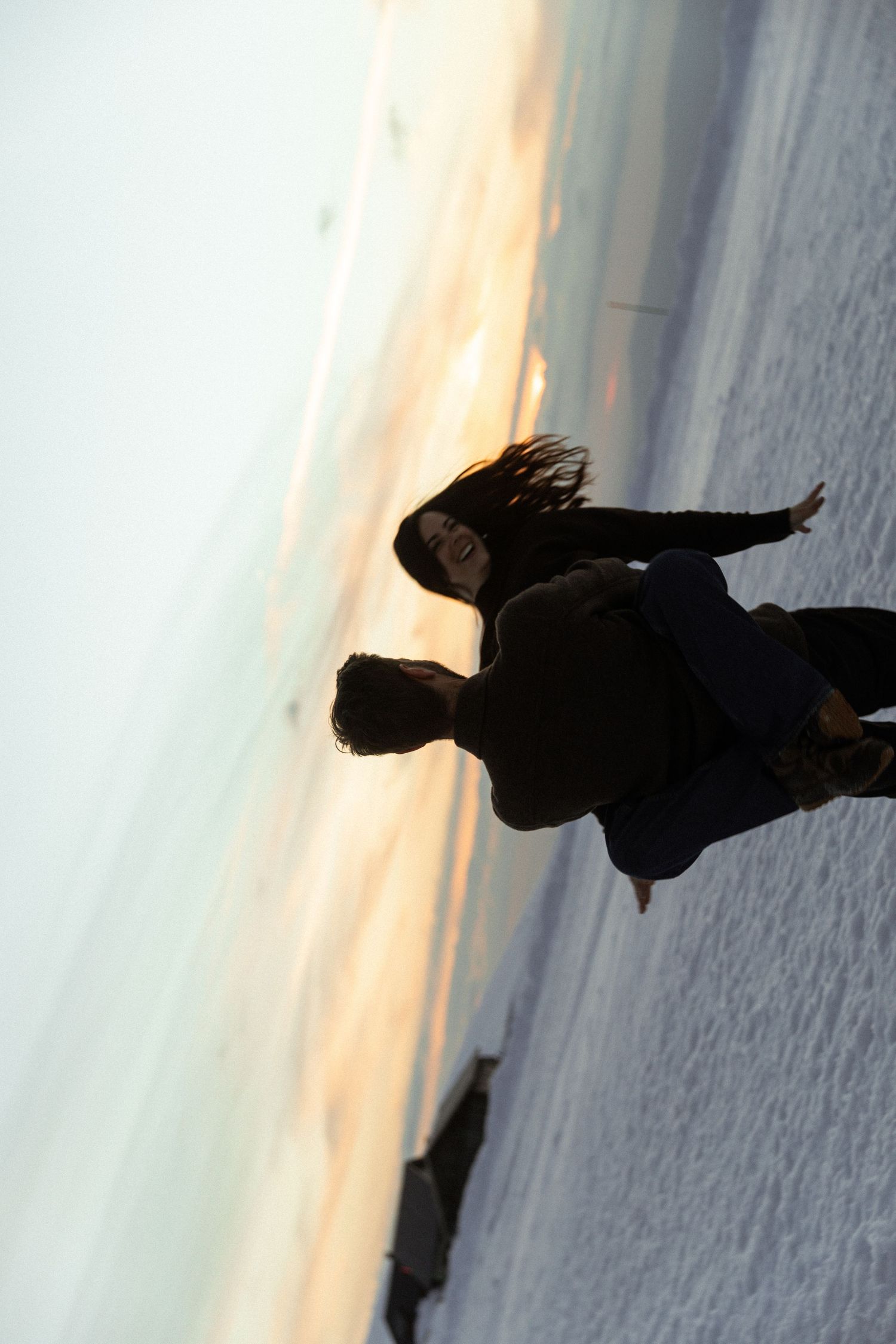 Silhouetted figure in black coat stands against a tilted horizon at sunset creating a dramatic artistic composition.