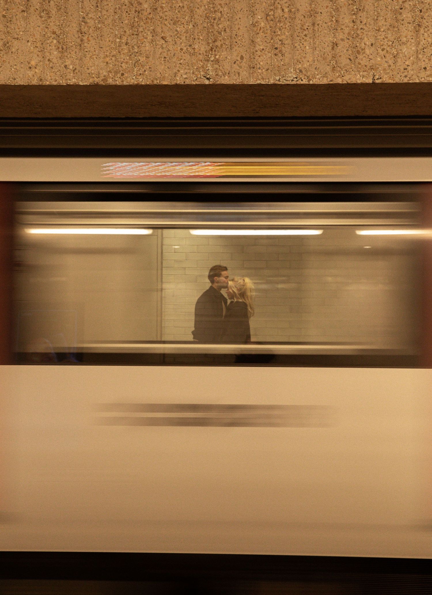 A blurred subway train passes by, revealing a couple standing on the platform through the window in a cinematic moment.